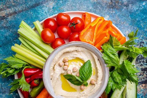 Hummus platter with assorted snacks. Hummus in bowl and vegetables sticks. Plate with Middle Eastern Party, finger food. Top view. Vegan, hummus dip